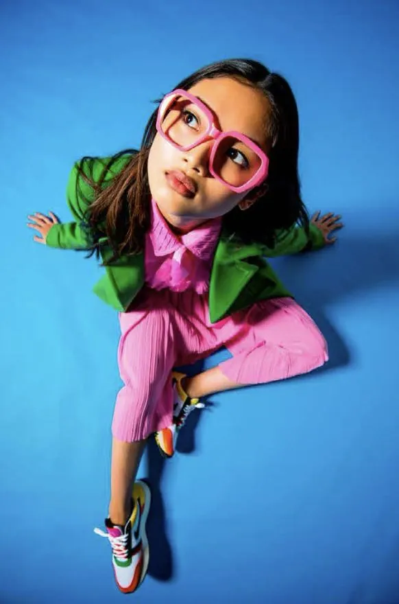 Child in pink glasses sitting on a blue floor